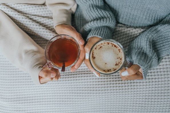 two sets of light skinned hands holding glasses of warm beverages